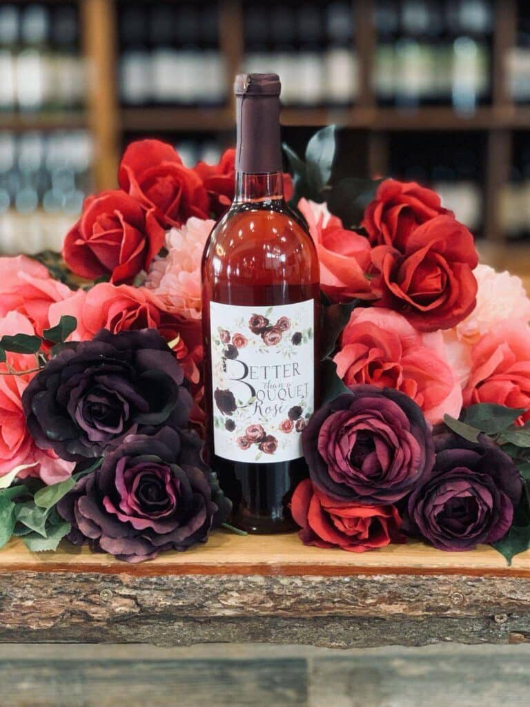 A bottle of better than a bouquet rose nestled in a bouquet of light and dark red roses.