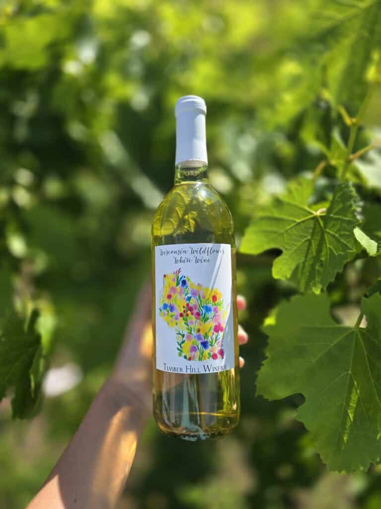 A bottle of Wisconsin Wildflower white wine being held up by tree leaves